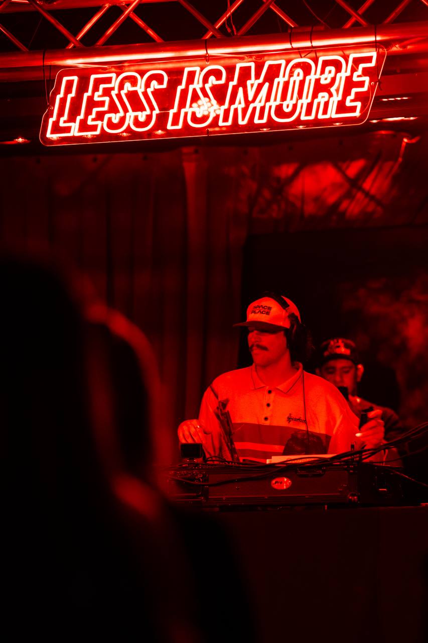 DJ under neon Less Is More sign