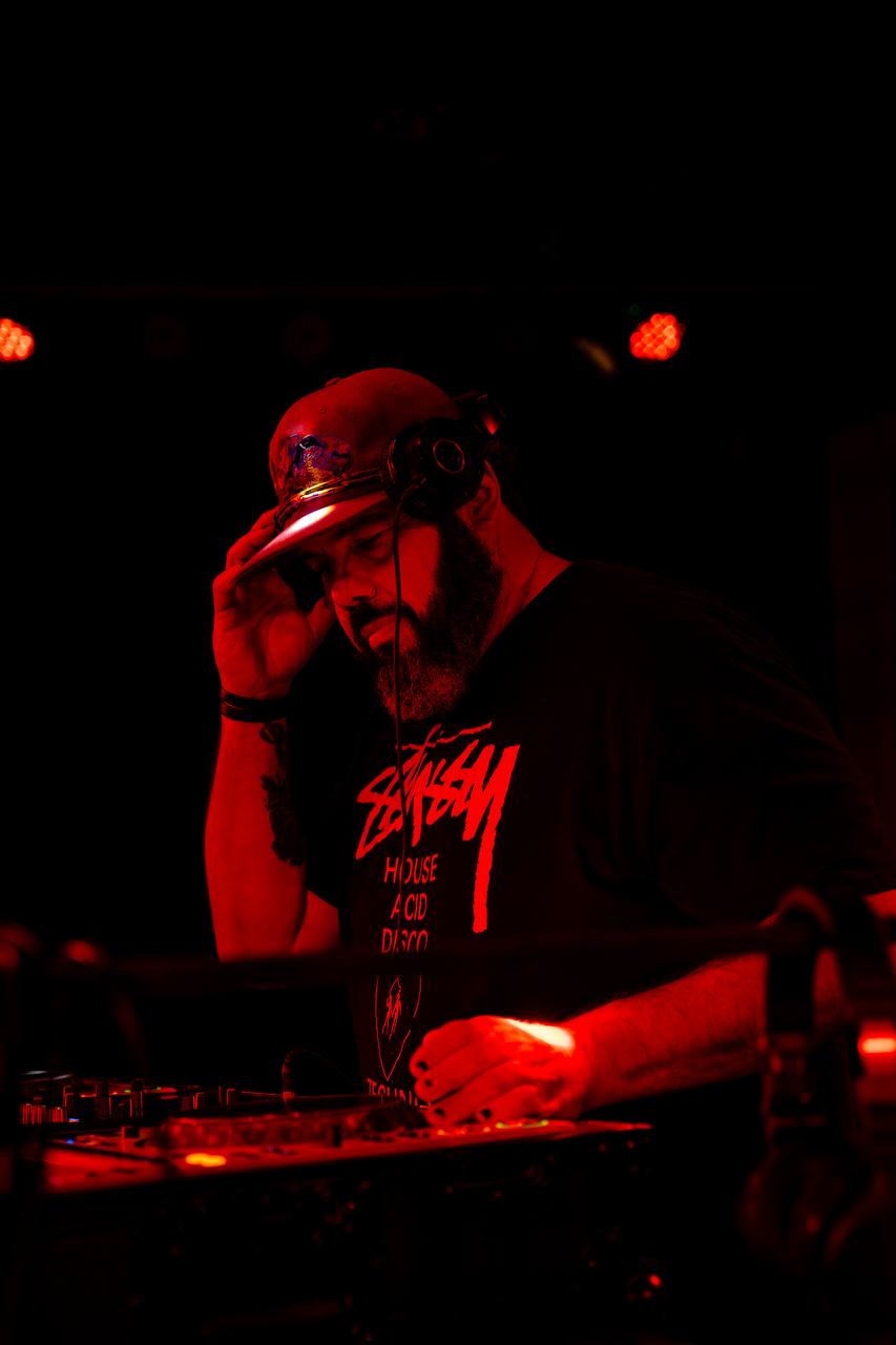 DJ in Stüssy tee, red lighting, hands on the mixer